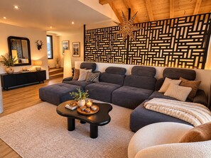 Un salon moderne avec un canapé d’angle, une table basse agrémentée d’objets décoratifs, un panneau mural à motifs et un plafond en bois.