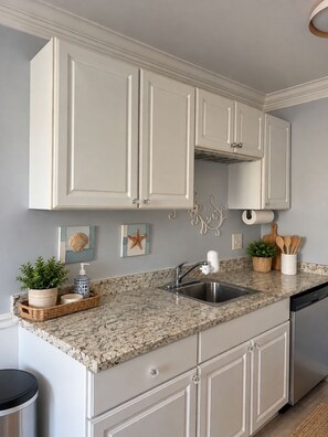 A kitchen with white cabinets, a granite countertop, a stainless steel sink, and a dishwasher. - Surf and Sand Retreat-Walk to Beach, Modern Amenities (Virginia Beach)