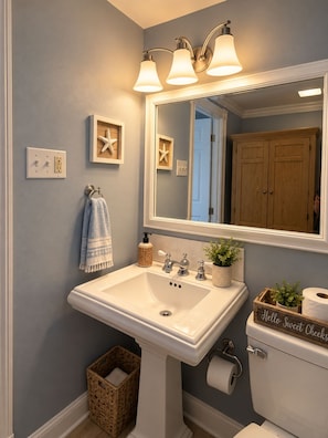 A bathroom with a white sink, a mirror, and a wooden cabinet. - Surf and Sand Retreat-Walk to Beach, Modern Amenities (Virginia Beach)