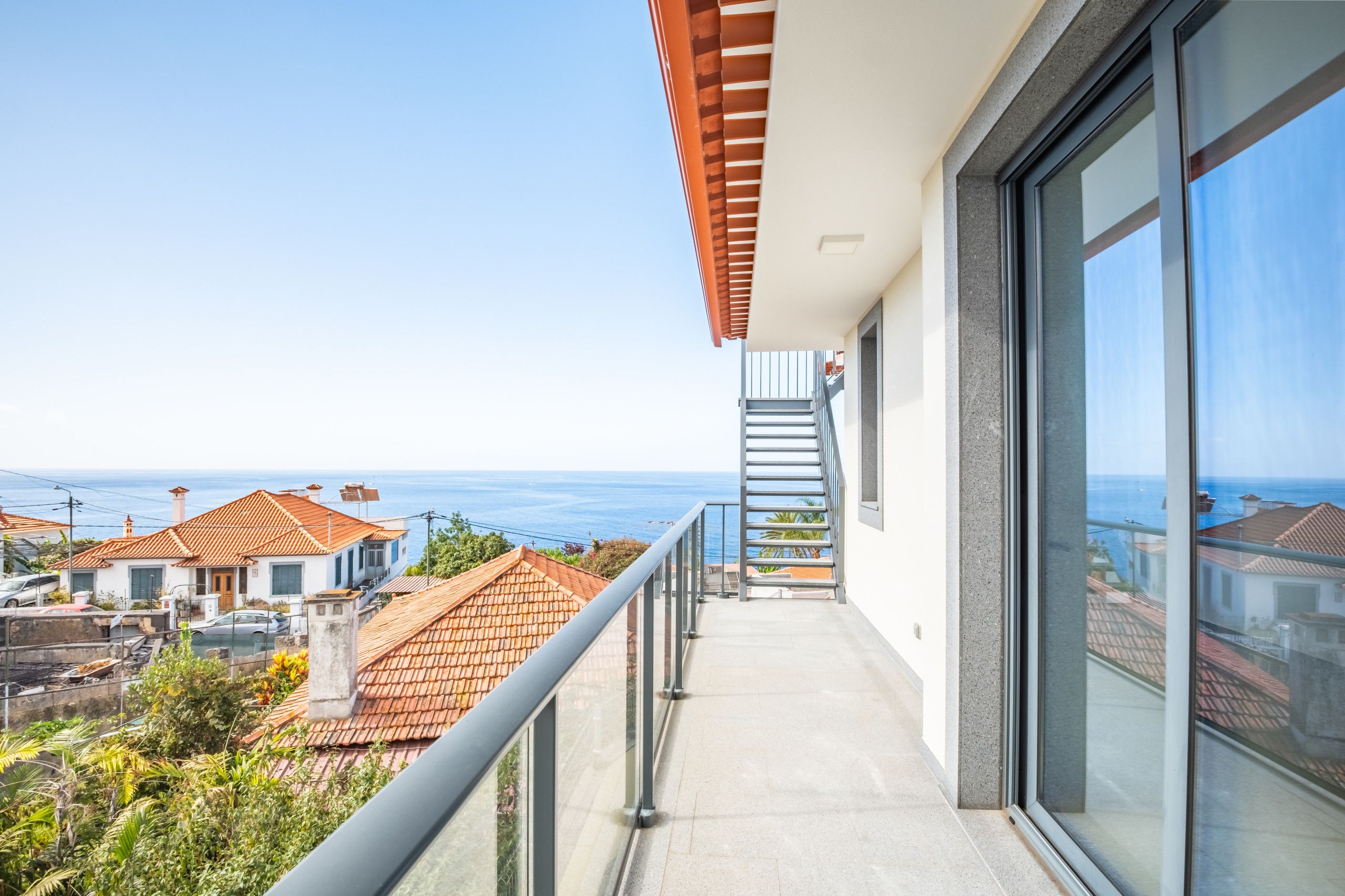 A balcony with a view of the sea, a staircase, and a glass door.
