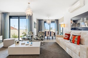 Un salon moderne avec un canapé blanc, une table basse et un lustre. On y trouve également un coin repas avec des chaises et une table.