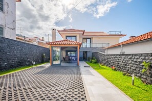 Una casa moderna con un porche cubierto, un muro de piedra y un jardín bien cuidado.