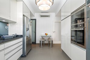 A modern kitchen with white cabinetry, a built-in oven, and a dining area with a table and chairs. - Villa Polaris by Homie (Funchal)