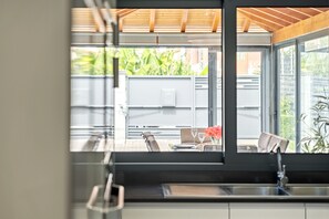 A modern kitchen with a large window, a dining area with a table and chairs, and a view of a garden. - Villa Polaris by Homie (Funchal)