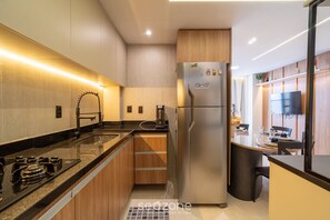 A modern kitchen with a stainless steel refrigerator, wooden cabinets, a black countertop, and a built-in oven. - Apt in Beachfront Building With Pool Hss0008 (João Pessoa)