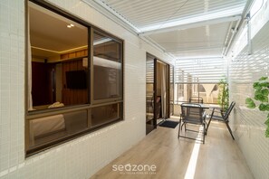 A corridor with a glass door leading to a room with a television, a tiled wall, and a seating area with a table and chairs. - Apt in Beachfront Building With Pool Hss0008 (João Pessoa)