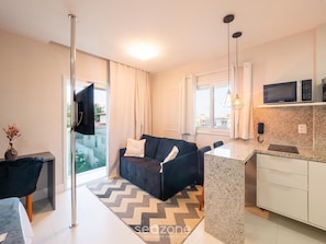 A modern living room with a sofa, a dining area, and a kitchen with a microwave. - Apart in Condo With Pool in Stella Maris Psp0107 (Salvador)