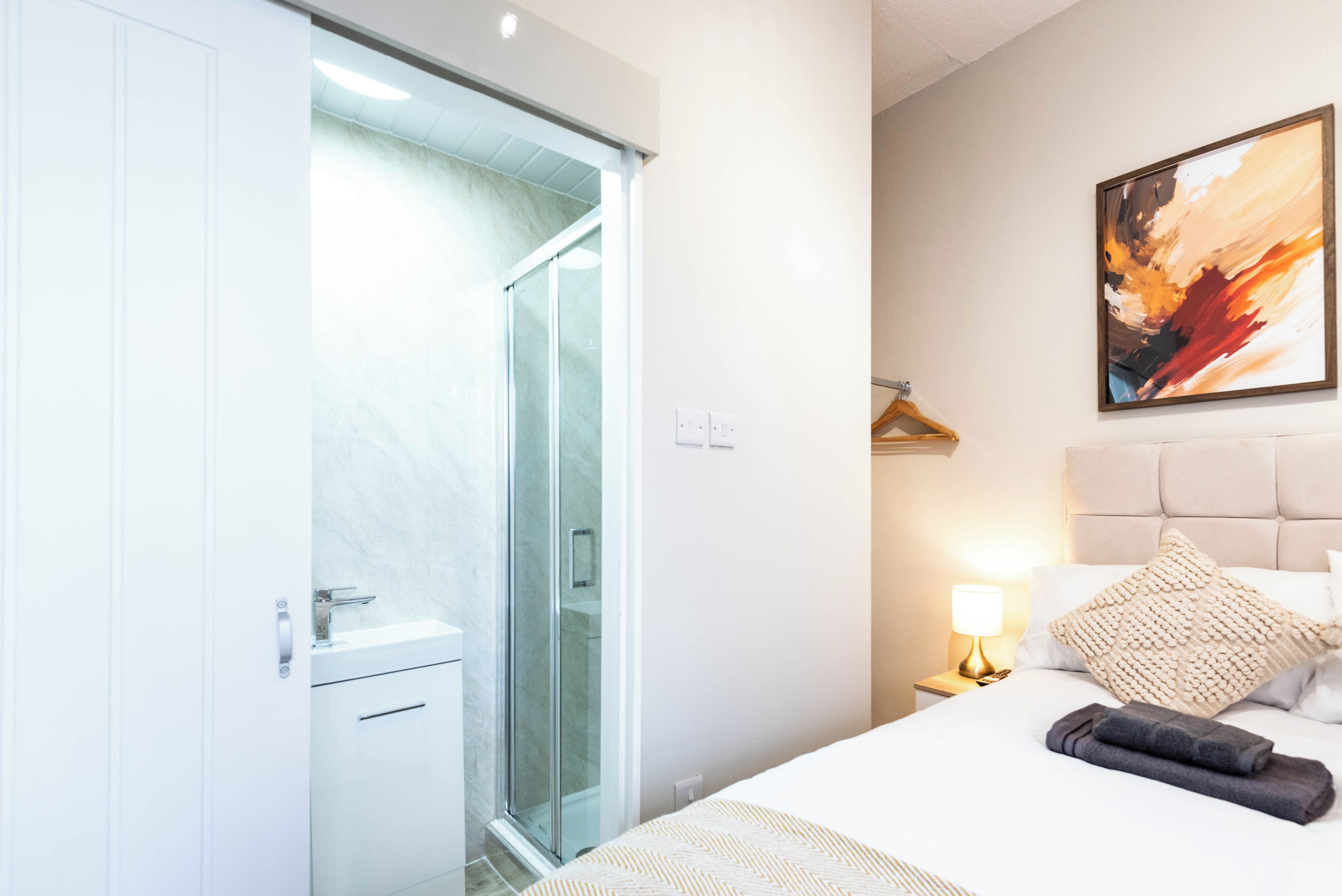 Une chambre d’hôtel avec un lit, une table de chevet, un tableau et une porte coulissante donnant sur une salle de bain.