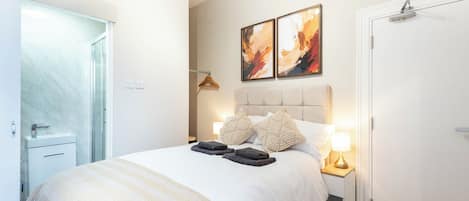 A bedroom with a bed, bedside lamps, a door, and a wall-mounted artwork.