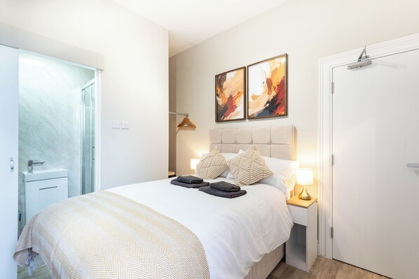 Un dormitorio con cama, lámparas de noche, una puerta y una obra de arte colgada en la pared.