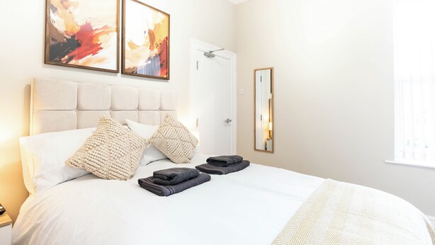 Ein Hotelzimmer mit einem großen Bett, zwei Kissen, einem gefalteten Handtuch, einem Spiegel und zwei abstrakten Bildern an der Wand.