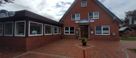 Ein Backsteinhaus mit einem dreieckigen Dach, einem Schild mit der Aufschrift 'Gasthaus-Pension Zum Elbblick' und einem gepflasterten Eingangsbereich.