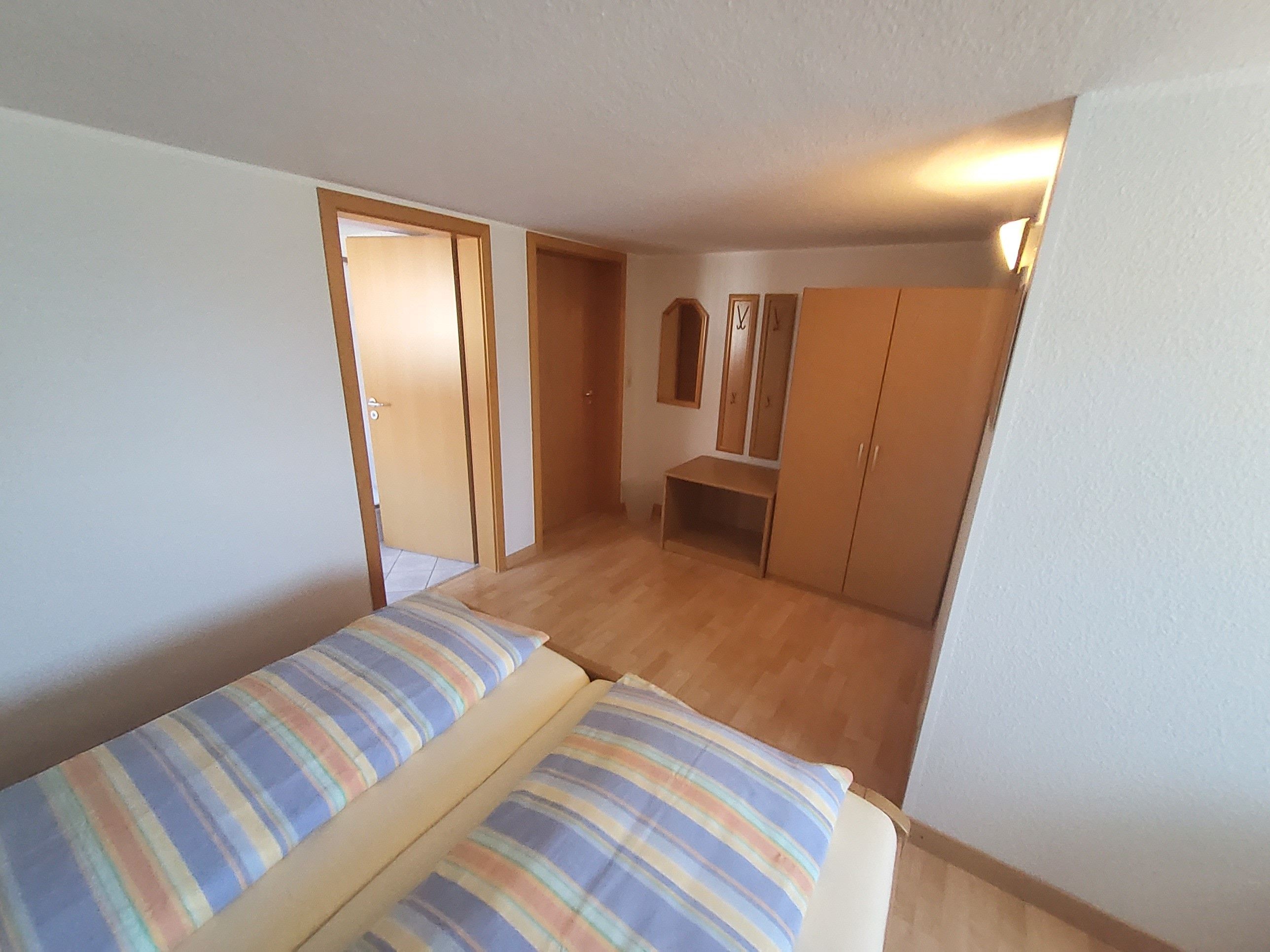 Een slaapkamer met een bed, een kledingkast, een spiegel en een deur naar een andere kamer.
