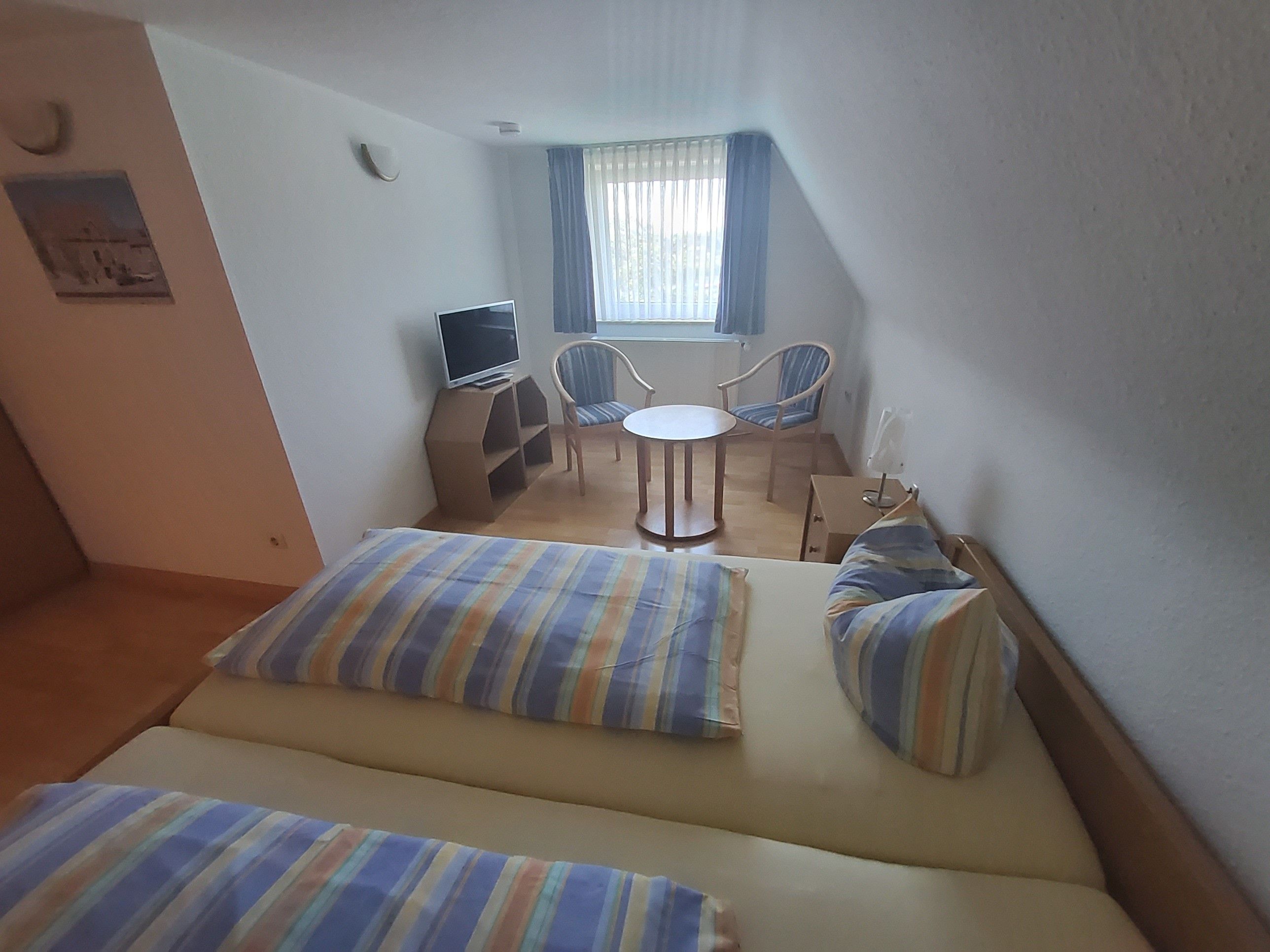 Une petite pièce, de taille modeste, comprenant un lit, un bureau, une chaise et un téléviseur.