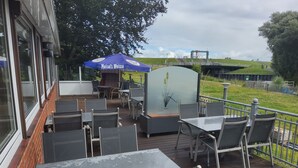 An outdoor patio with tables and chairs, a blue umbrella, and a decorative wall. - Room 'Zum Elbblick – Double Room No. 18' with Sea View, Terrace & Wi-Fi (Otterndorf)