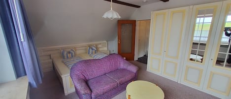 Une chambre à coucher avec un lit, un canapé violet, une petite table ronde et une armoire aux portes en verre.