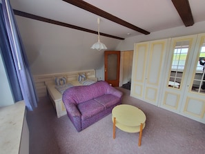 A bedroom with a bed, a purple sofa, a small round table, and a wardrobe with glass doors.