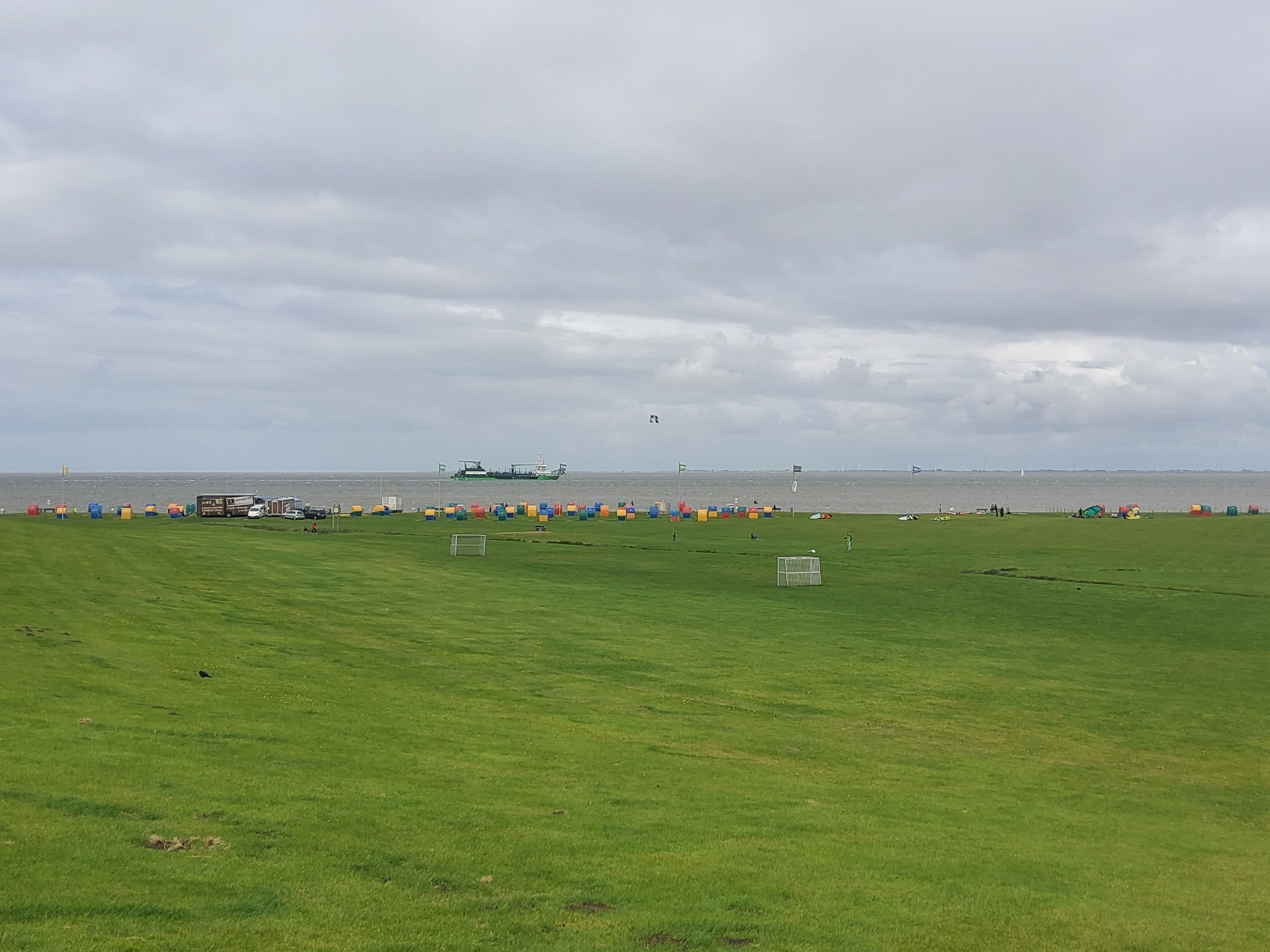 A grassy field with a soccer goal, a boat in the water, and a cloudy sky.