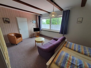 A room with a sofa, a chair, a small table, a television, and a window with curtains.