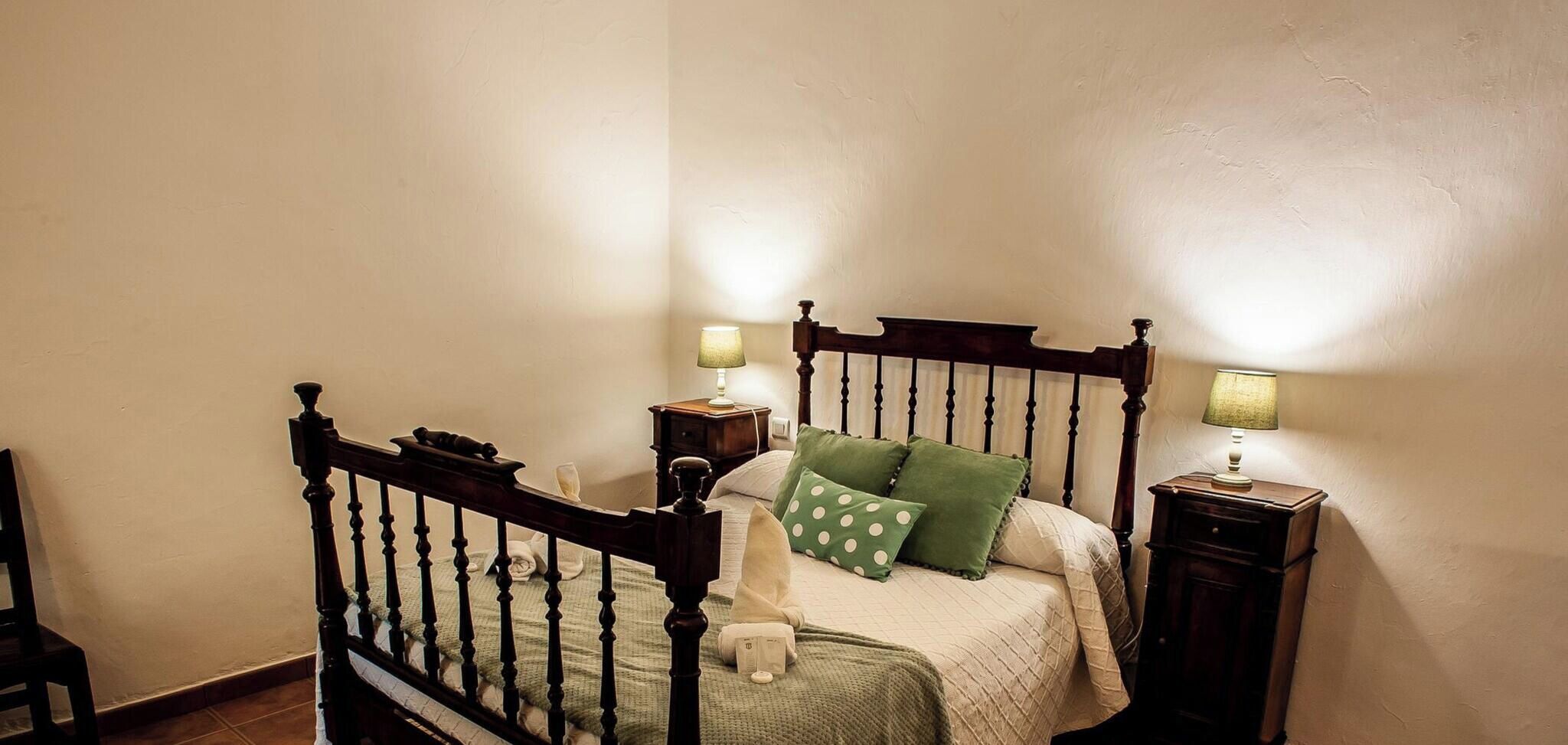 Une chambre à coucher avec un lit à baldaquin en bois, deux tables de chevet avec des lampes et un coussin à pois verts.