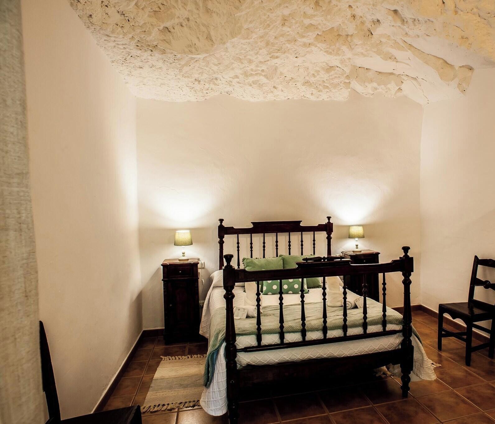 A bedroom with a four-poster bed, two bedside tables, a chair, and a lamp on each side of the bed.