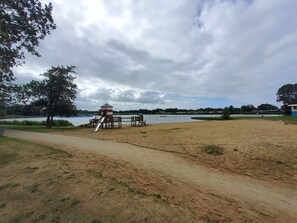 A sandy beach area with a small wooden structure, possibly a playhouse, near a body of water.