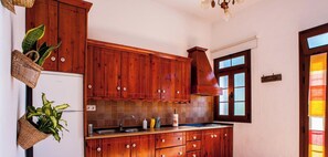 A kitchen with wooden cabinets, a sink, and a window with frosted glass panels. - Cave Retreat for 3 guests (Artenara)