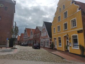 A cobblestone street lined with traditional half-timbered houses, a parked car, and a visible parking sign.