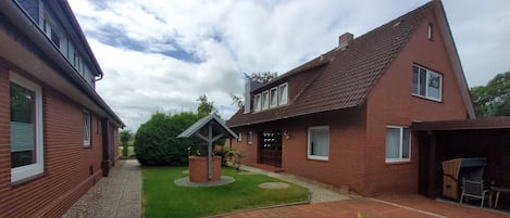 A courtyard with a paved area, a small garden, and a brick house with a pitched roof.