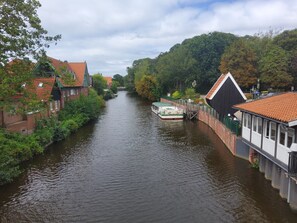 A narrow waterway flanked by buildings with red-tiled roofs, a boat docked on the right, and a bridge in the distance.