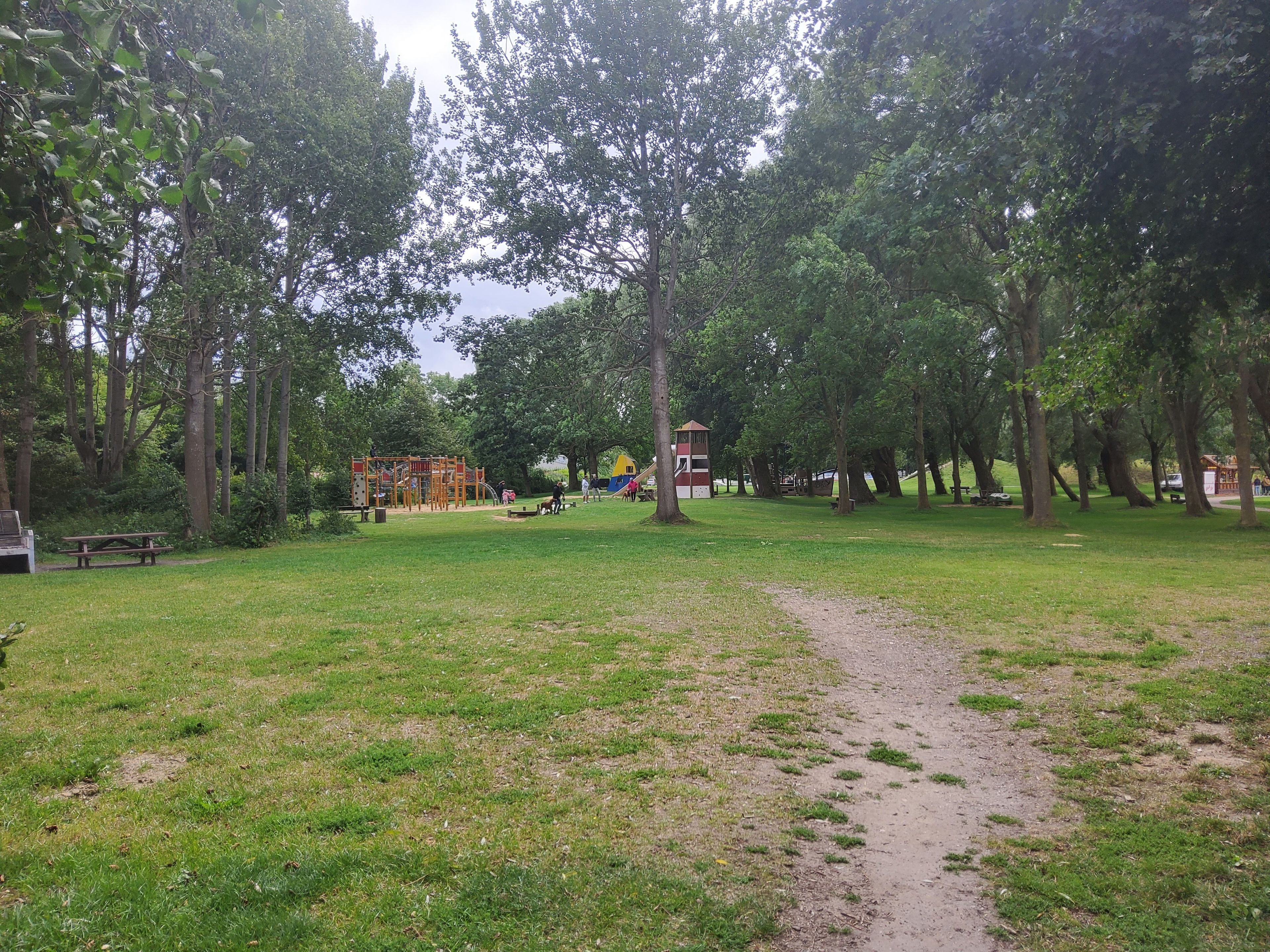 Een park met een speeltuin, picknicktafels en een pad van aarde.