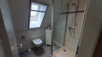 Un baño con inodoro, ducha y tragaluz.