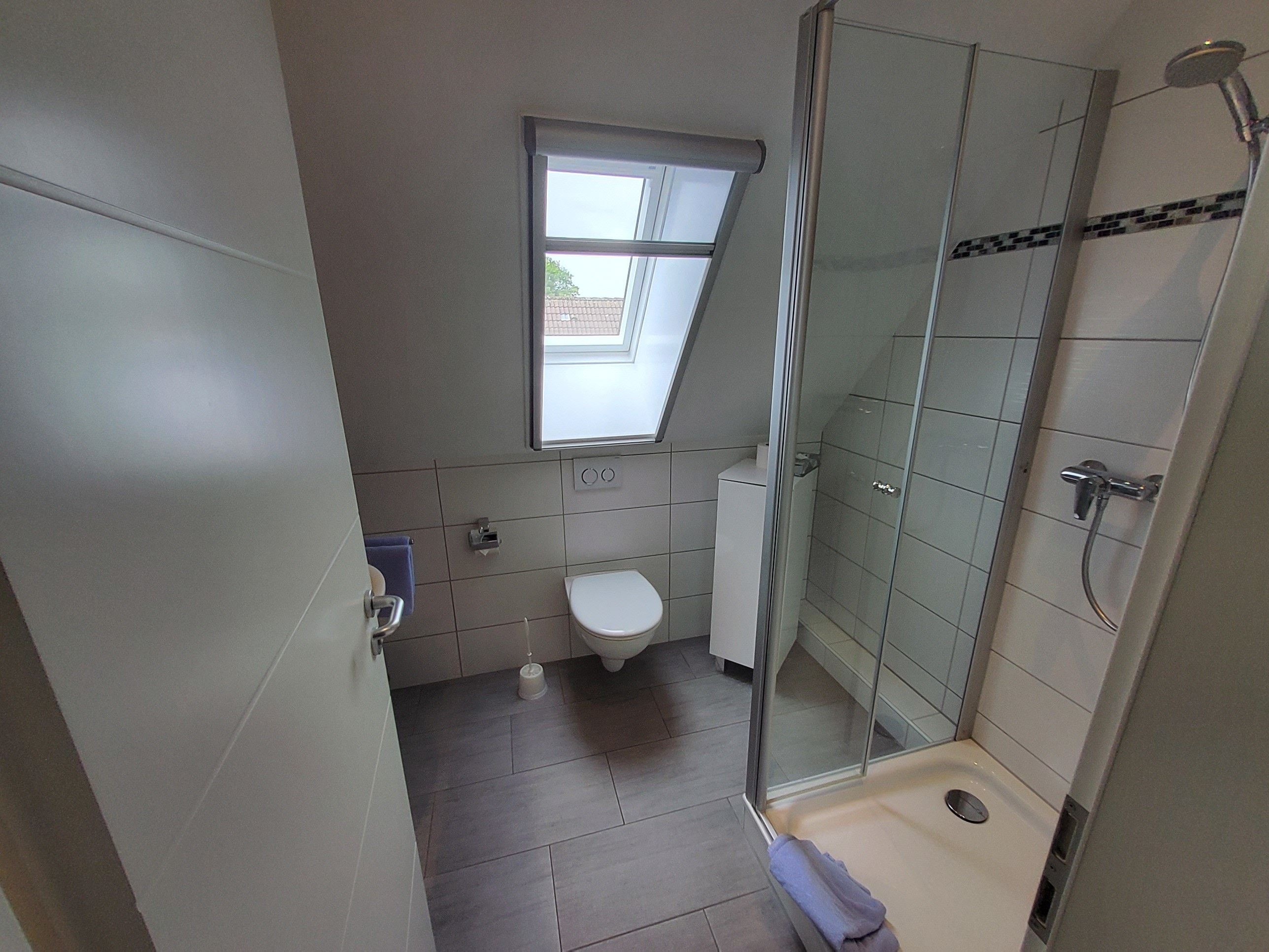 A compact bathroom with a toilet, a shower enclosure, and a window providing natural light.