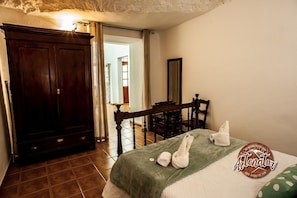 A bedroom with a bed, a wooden wardrobe, a desk, and a mirror. - Cave Stay near Mountain (Artenara)