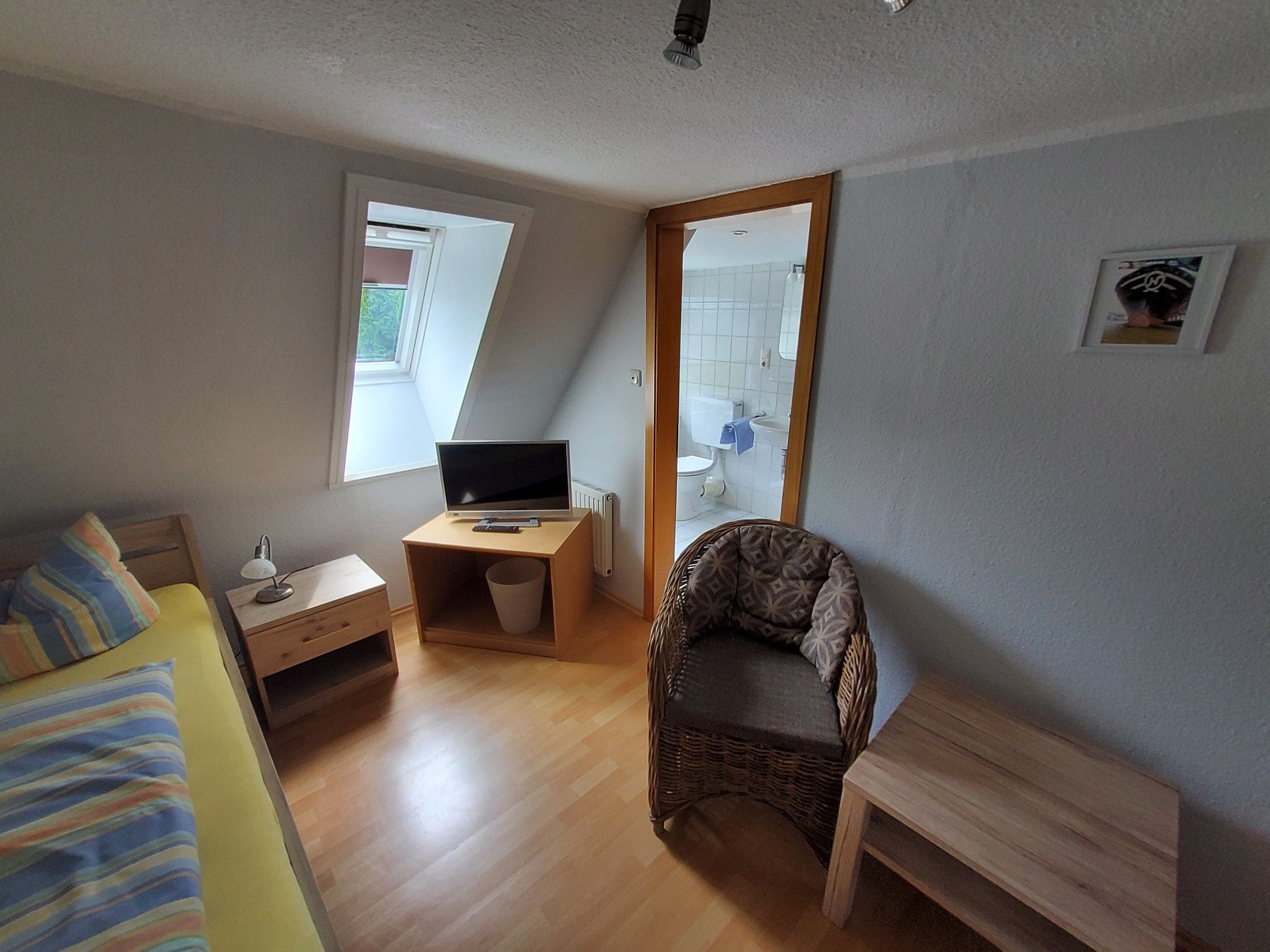 A small, compact room with a bed, a desk with a computer, a chair, and a window.