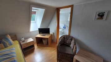 Ein kleines, kompaktes Zimmer mit einem Bett, einem Schreibtisch mit Computer, einem Stuhl und einem Fenster.
