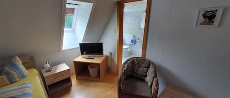 Une petite pièce, de taille modeste, comprenant un lit, un bureau avec un ordinateur, une chaise et une fenêtre.