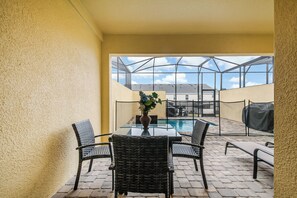 Ein Tisch mit Glasplatte, vier Korbstühle, eine Vase mit Blumen und Blick auf einen Swimmingpool durch eine Glasverkleidung.