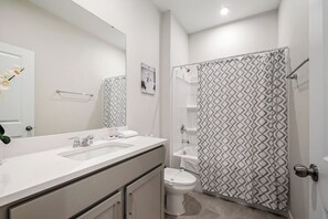 Ein Badezimmer mit einem weißen Waschbecken, einer Toilette, einer Dusche mit gemustertem Vorhang und einem Spiegel.