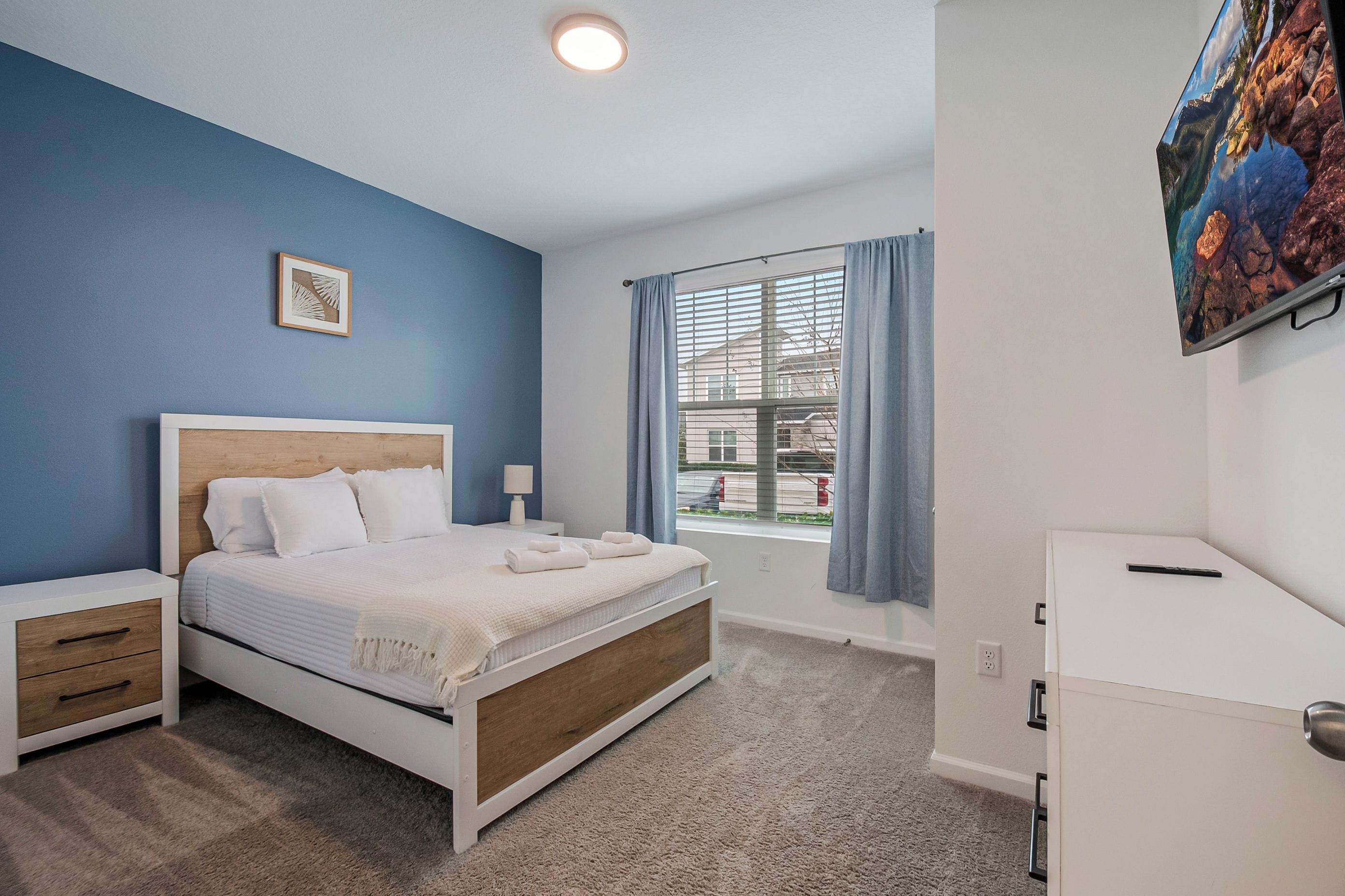 A bedroom with a bed, a bedside table, a lamp, a window with curtains, and a painting on the wall.