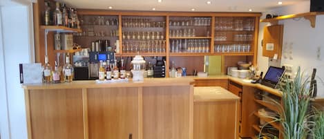 Eine Bar mit Holztresen, Regalen mit Gläsern und einem Laptop auf dem Tresen.