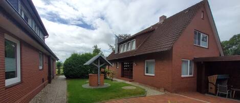 A courtyard with a paved area, a small garden, and a brick house with a pitched roof.