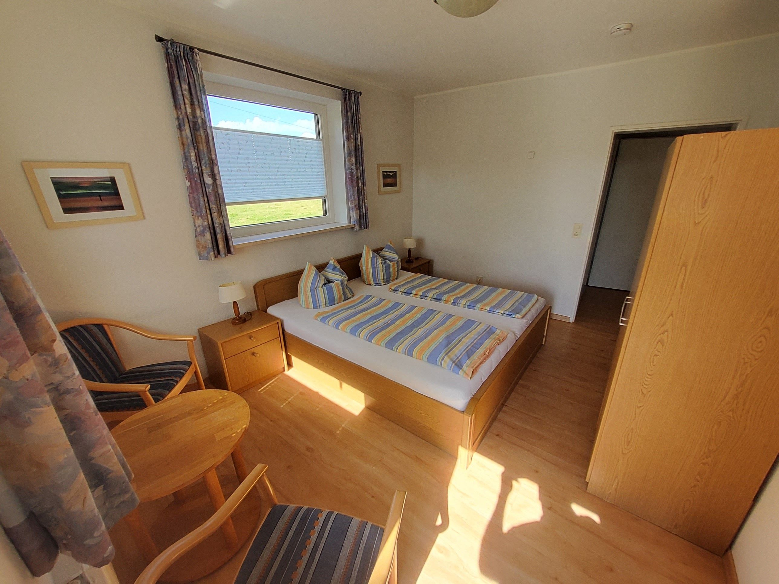 A bedroom with a bed, a chair, a nightstand, a window with curtains, and a door.