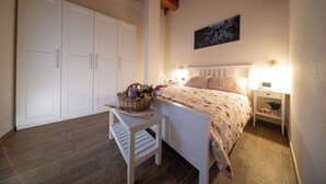 A bedroom with a bed, bedside tables, a nightstand, a chair, a wooden beam ceiling, and a wardrobe. - Pulsatilla - two-room apartment with balconies (Closellinaz)