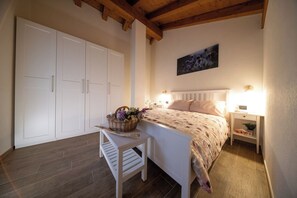 Une chambre à coucher comprenant un lit, des tables de chevet, une commode, une chaise, un plafond avec poutres apparentes en bois et une armoire.