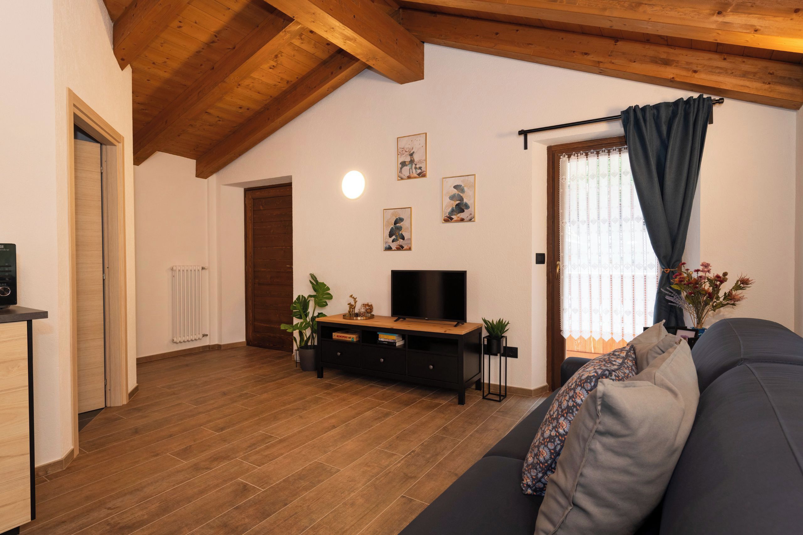 Ein Wohnzimmer mit Holzboden, einem schwarzen Sofa, einem Fernseher auf einem Holzständer und einer Heizung.