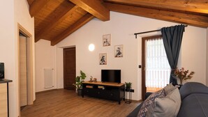 A living room with a wooden ceiling, a black sofa, a TV on a wooden stand, and a radiator. - Pulsatilla - two-room apartment with balconies (Closellinaz)