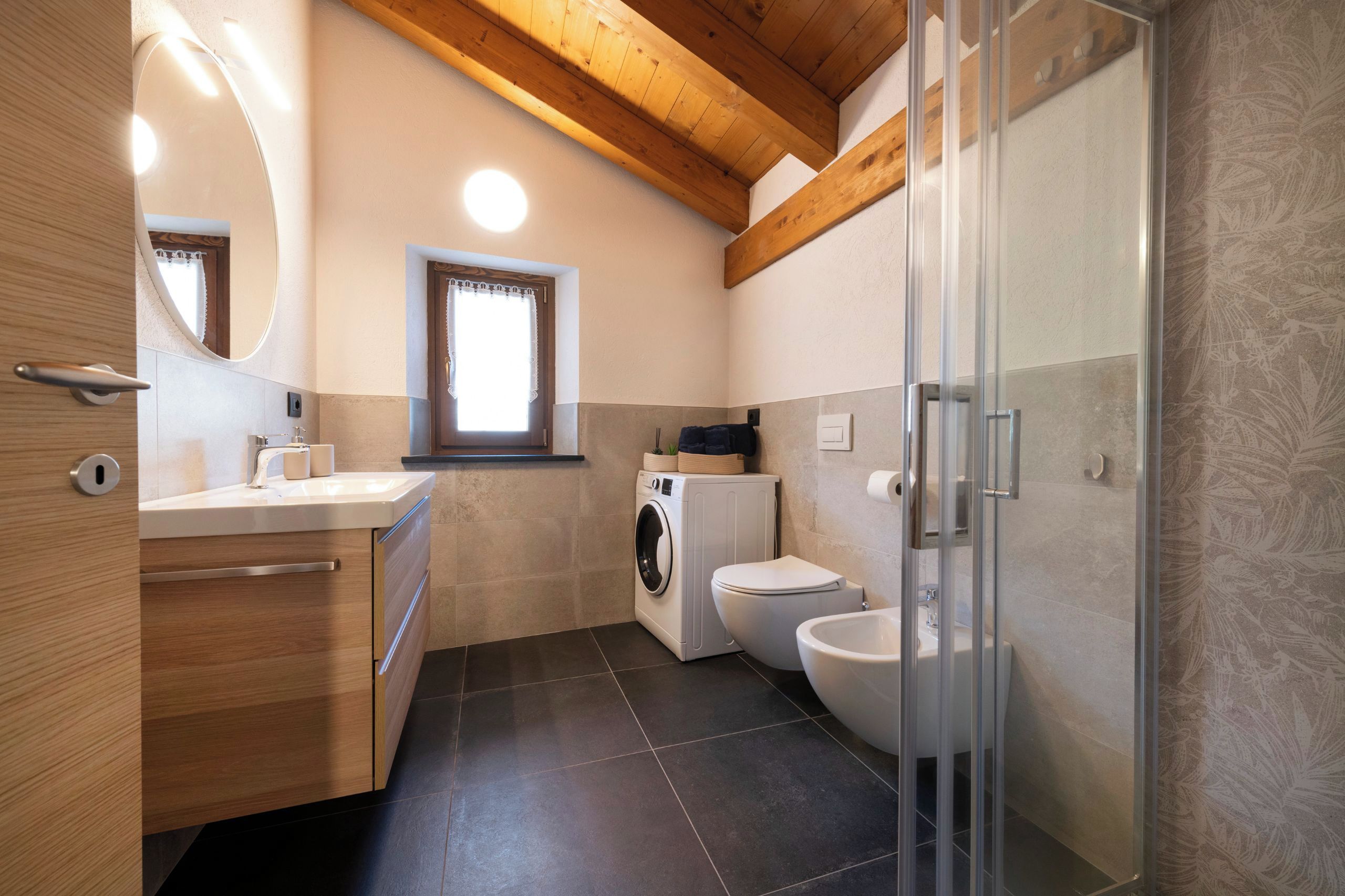 A modern bathroom with a wooden ceiling, a built-in washing machine, a toilet, and a glass shower enclosure.