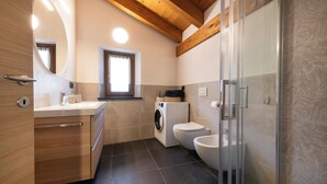 A modern bathroom with a wooden ceiling, a built-in washing machine, a toilet, and a glass shower enclosure. - Pulsatilla - two-room apartment with balconies (Closellinaz)