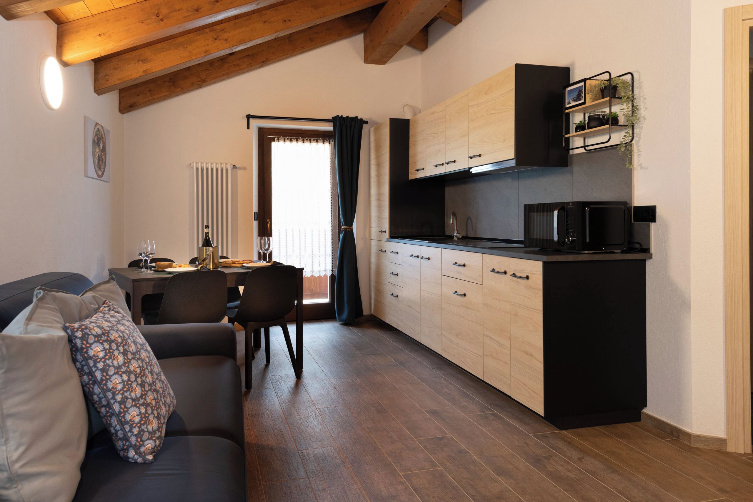 Un ambiente compatto con angolo cottura, zona pranzo e divano con cuscini decorati.
